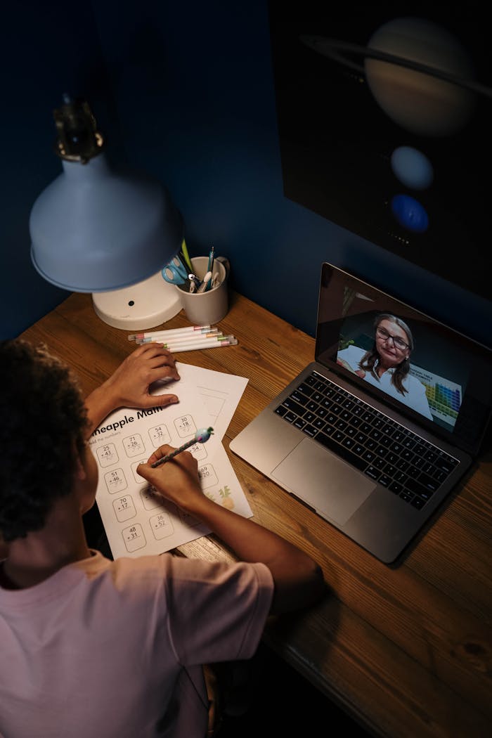 Child engaged in online learning session with a teacher via laptop.